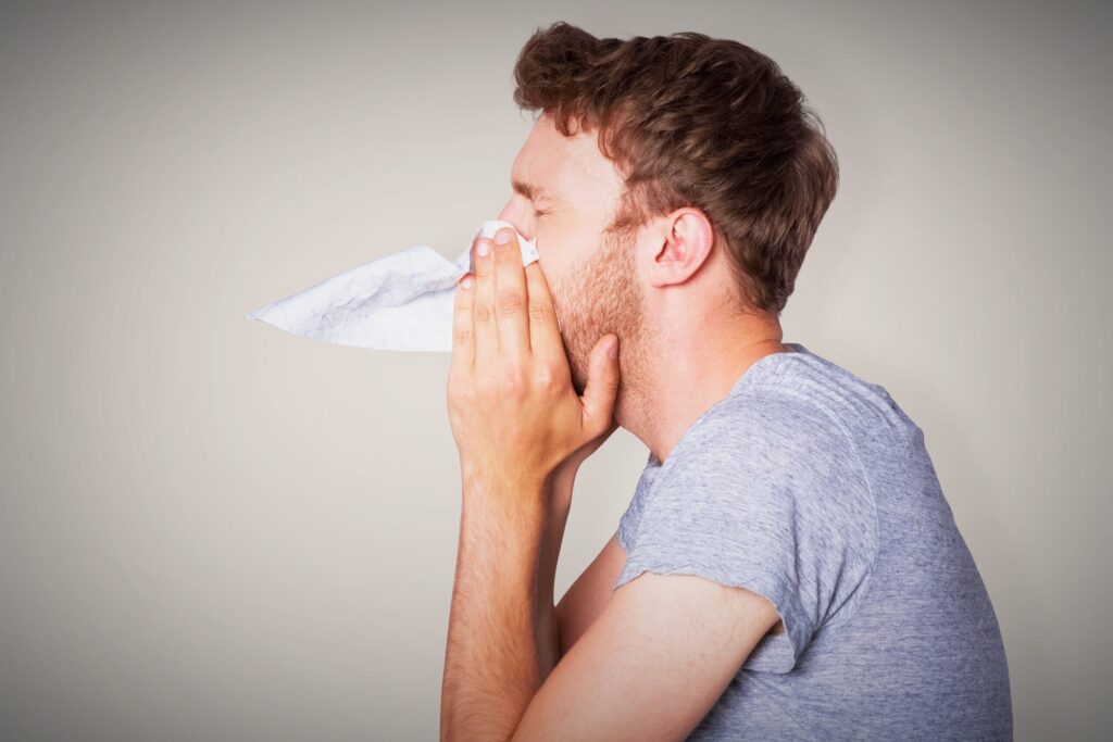 man blowing nose into tissue