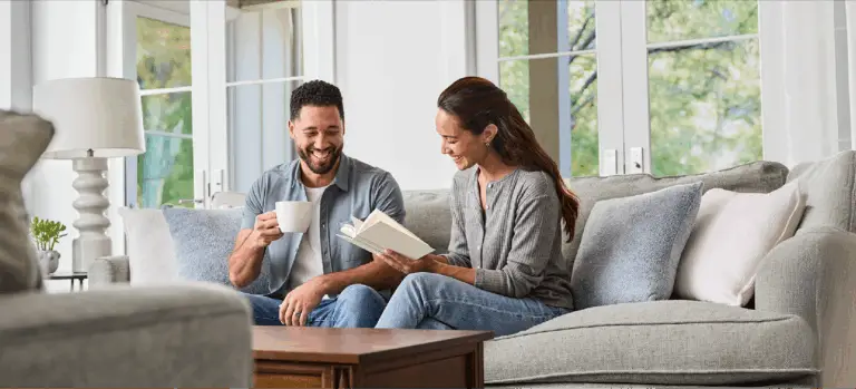 A couple on the sofa, drinking coffee and reading a book.